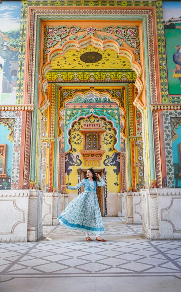 A woman in a traditional Indian dress twirls happily in front of the vibrantly colored and intricately painted archways of Patrika Gate in Jaipur, Rajasthan.